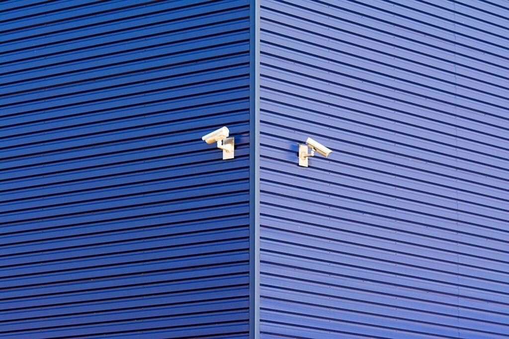 Minimalist image of a blue wall with two CCTV cameras emphasizing security and technology.